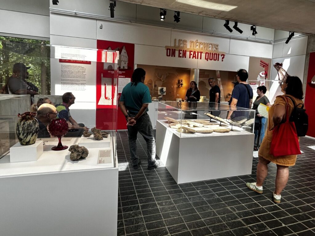Des visiteurs découvrent une exposition dans un musée, autour de vitrines présentant des objets et des panneaux explicatifs.