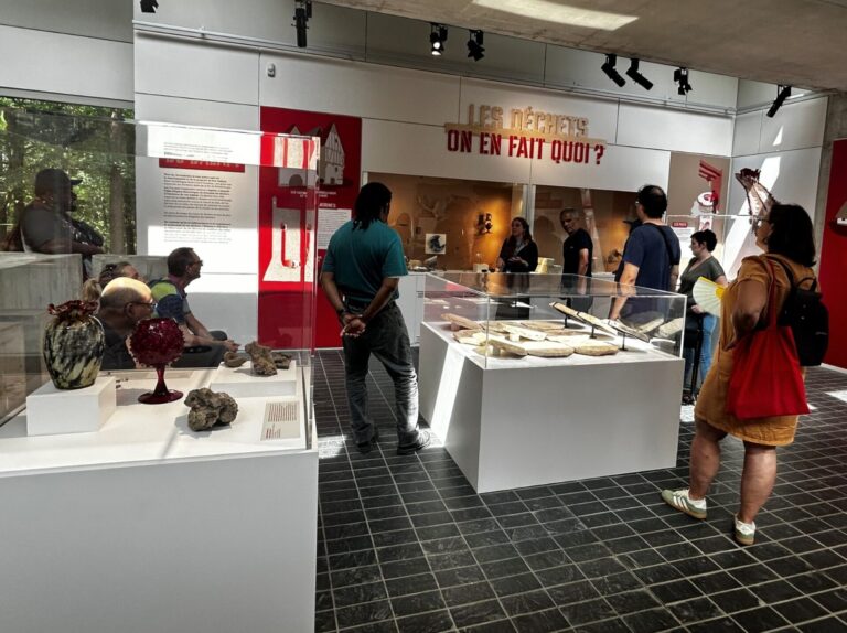 Des visiteurs découvrent une exposition dans un musée, autour de vitrines présentant des objets et des panneaux explicatifs.